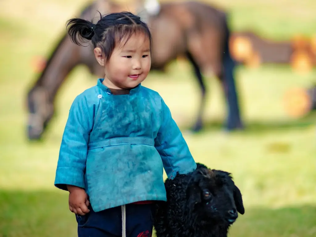 Mongolian child with a lamb, in the background a horse grazes