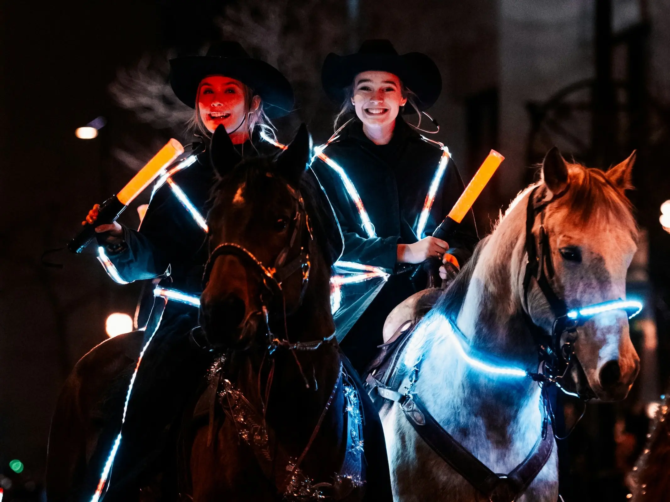 Smiling young women riding horses at night, wearing LEDs on their bridle