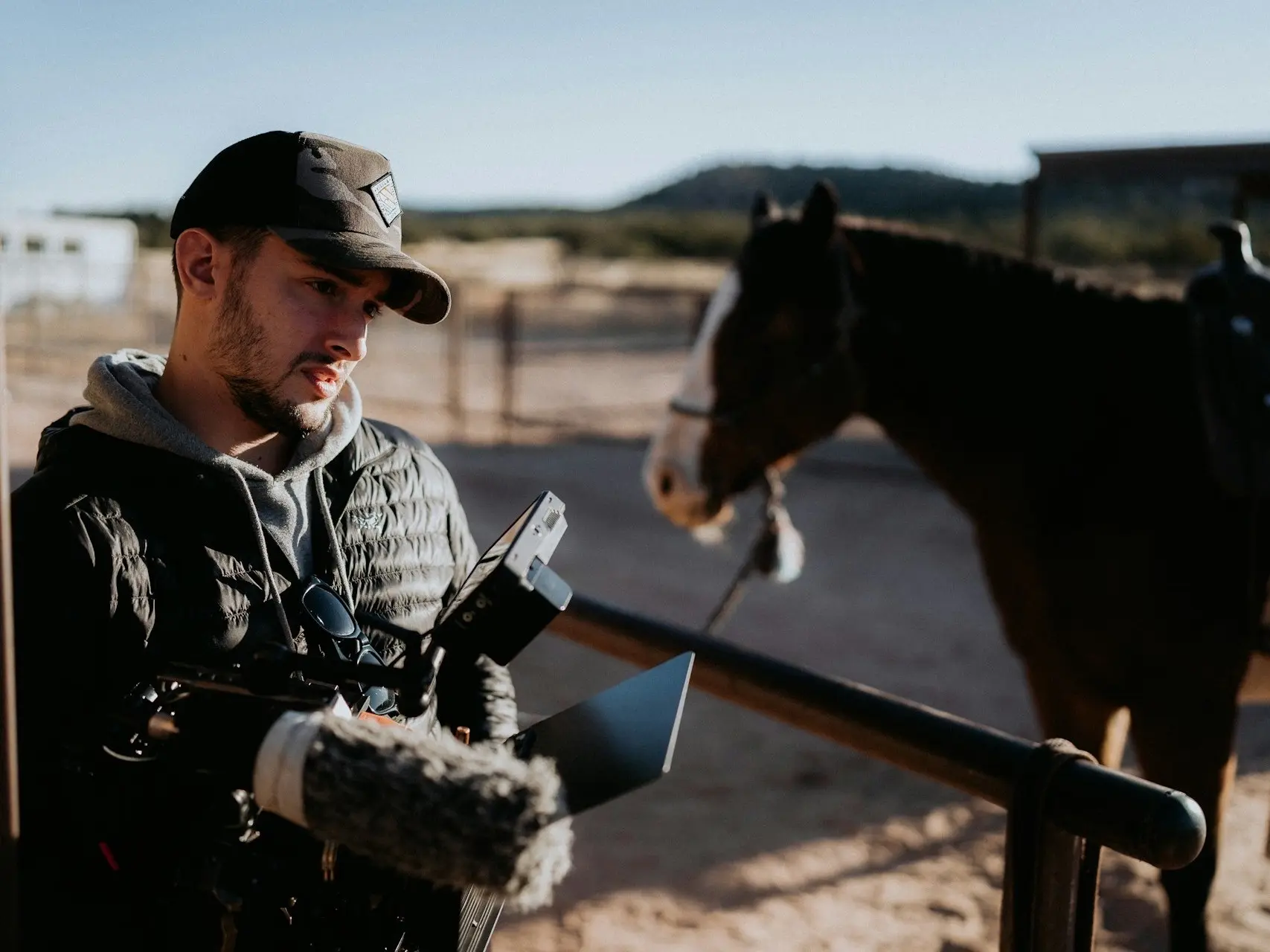 Man carrying computer and camera equipment past a horse